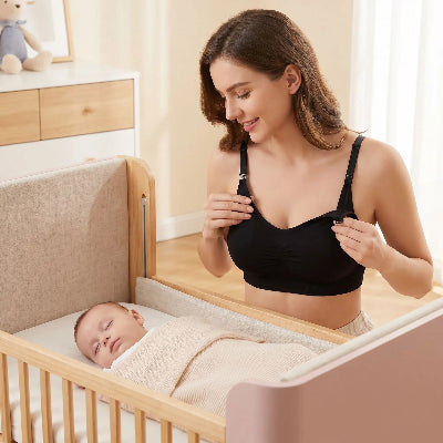 Une femme porte son soutien gorge allaitement grande taille Laflex noir et regarde son bébé dans son berceau