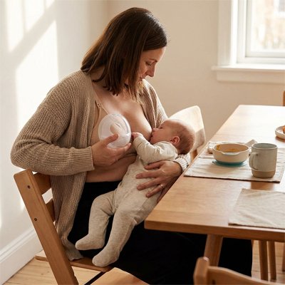 Une maman tête son  au sein gauche et a sa coquille d'allaitement sur son sein droit